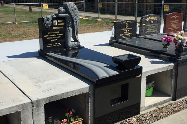 SX Black single vault with Angel headstone with gold incised inscription, base, flat ledger with raised sandblasted wave and planter box, front veneer with cabinet insert.